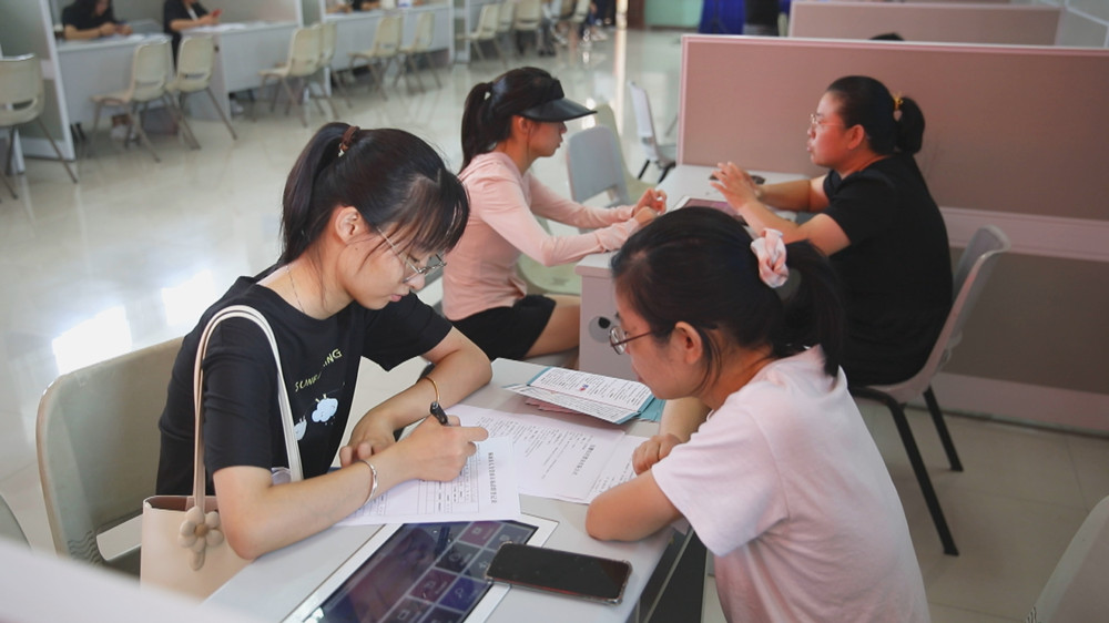 圖為高校畢業(yè)生汪戀(左一）正在一邊咨詢應聘職位信息一邊填寫應聘登記表.jpg