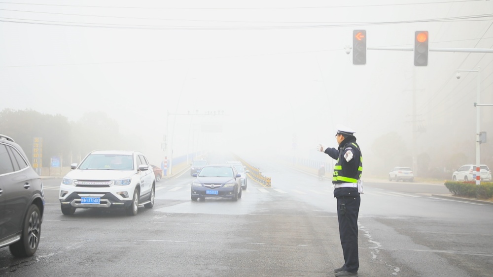 圖為執(zhí)勤民警正在大霧中指揮過(guò)往車輛有序通行.jpg